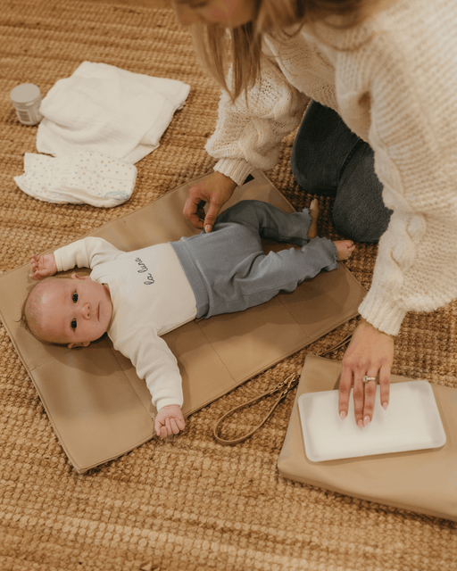 A mum changing her baby boy's nappy on the living room floor.